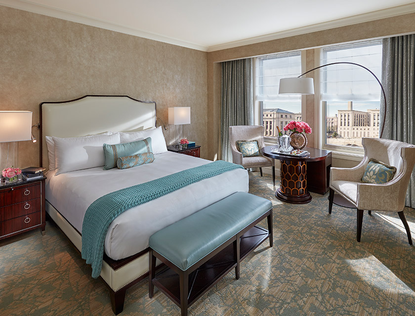 A white bed with a blue chair at the foot of the bed