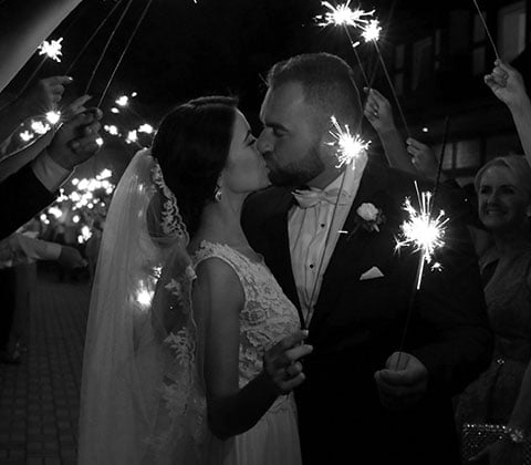 Couple kissing in wedding attire surrounded by their friends and family holding sparklers